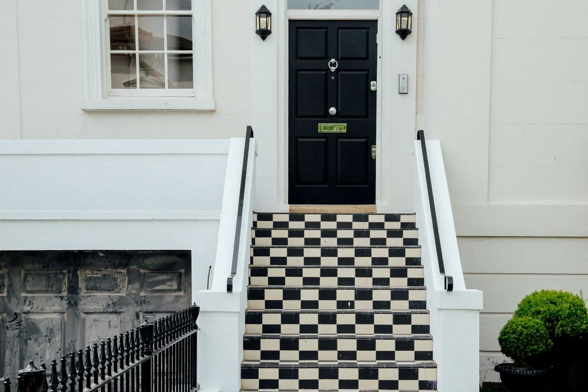 Glossy black front door with chequered tiled steps and white stucco