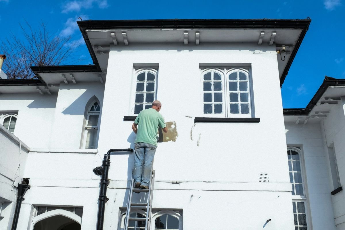 Decorator on a ladder painting a white rendered house exterior