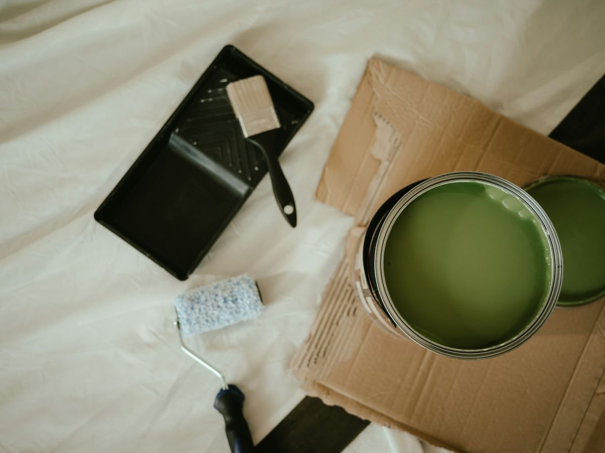 Open tin of sage green paint, roller and tray on a dust sheet