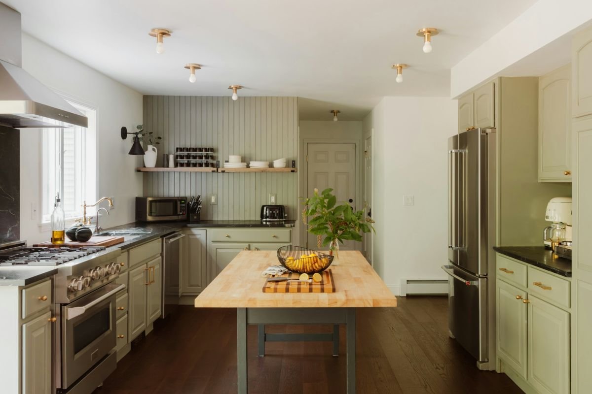 Kitchen with sage green painted cupboards and a wooden worktop